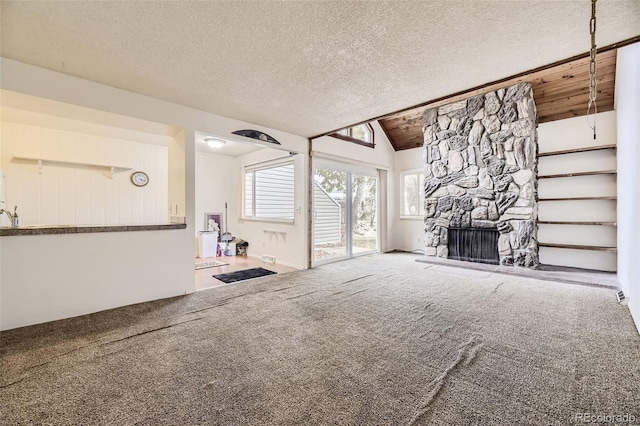 unfurnished living room with a stone fireplace, a textured ceiling, carpet flooring, and vaulted ceiling