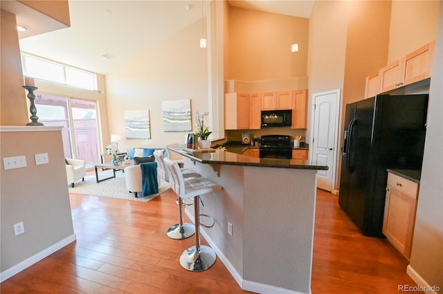 kitchen with kitchen peninsula, a kitchen breakfast bar, black appliances, high vaulted ceiling, and dark hardwood / wood-style floors