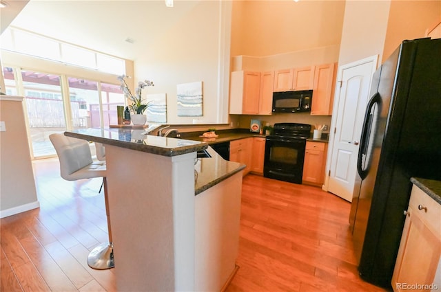 kitchen featuring kitchen peninsula, a towering ceiling, light wood-type flooring, black appliances, and a breakfast bar area