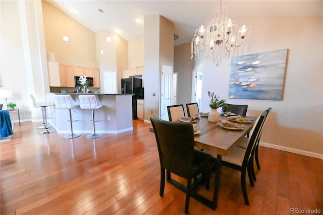 dining area featuring a chandelier, high vaulted ceiling, light wood-style flooring, and baseboards