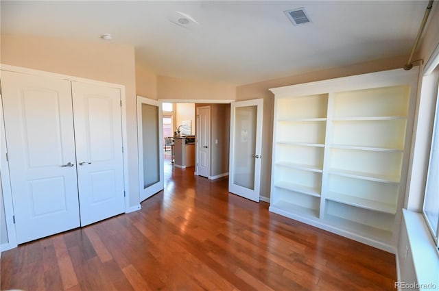 unfurnished bedroom with french doors, a closet, and dark wood-type flooring