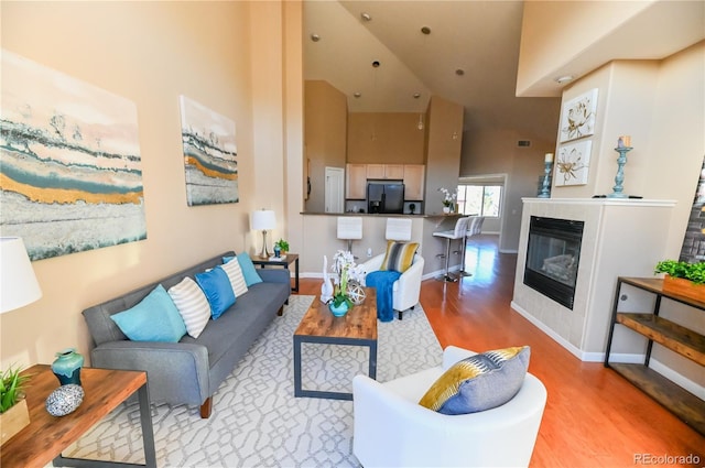 living room featuring a high ceiling, a fireplace, wood finished floors, and baseboards