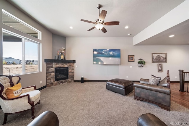 carpeted living room featuring a stone fireplace and ceiling fan