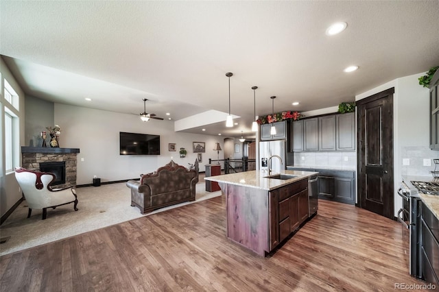 kitchen with a stone fireplace, pendant lighting, an island with sink, sink, and dark brown cabinets