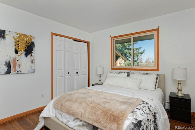 bedroom with a closet, a baseboard heating unit, baseboards, and wood finished floors