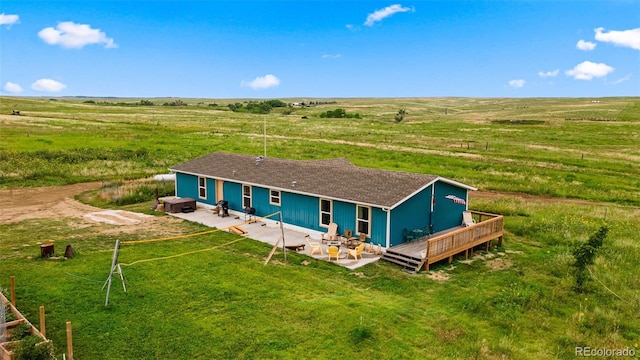 back of house featuring a rural view, a wooden deck, a lawn, and a patio