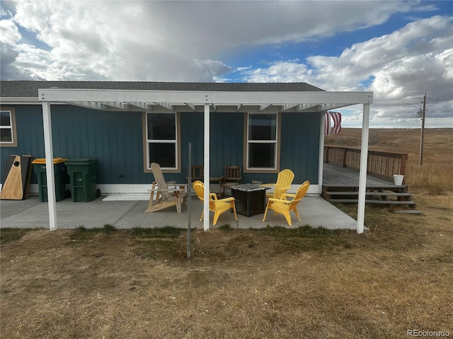 rear view of house with a wooden deck, a patio area, and an outdoor fire pit