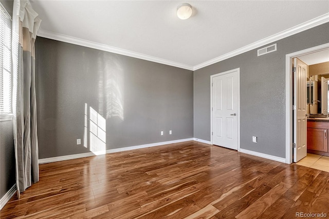 unfurnished bedroom with connected bathroom, crown molding, and hardwood / wood-style flooring