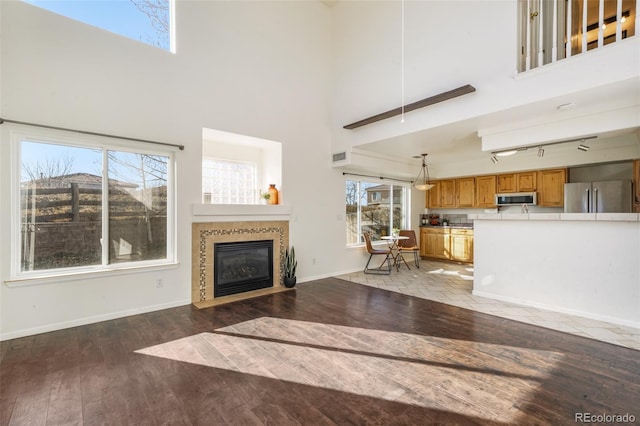 unfurnished living room with baseboards, a tile fireplace, wood finished floors, rail lighting, and a high ceiling