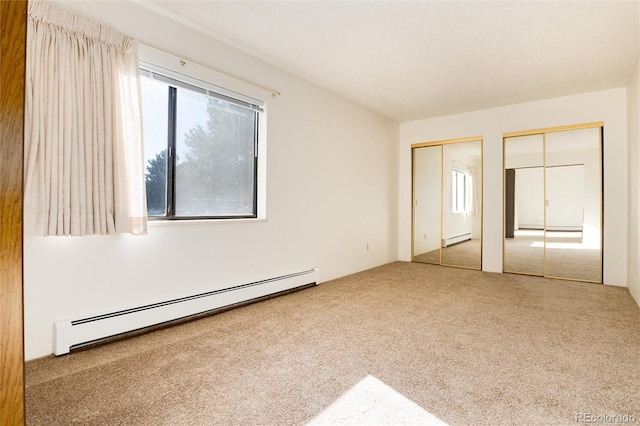 unfurnished bedroom featuring baseboard heating, multiple closets, and light carpet