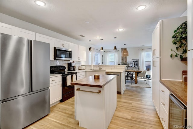 kitchen with stainless steel appliances, butcher block countertops, beverage cooler, a kitchen island, and pendant lighting