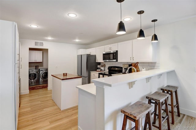 kitchen featuring white cabinets, independent washer and dryer, a kitchen bar, kitchen peninsula, and appliances with stainless steel finishes