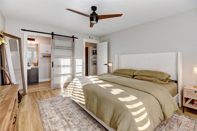 bedroom with ceiling fan, light hardwood / wood-style floors, and a barn door