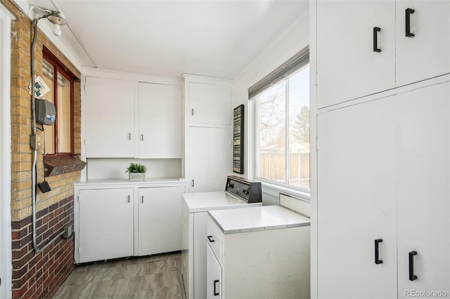 washroom featuring cabinets, washing machine and clothes dryer, and brick wall