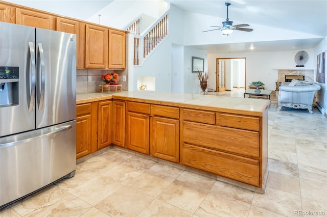 kitchen featuring a fireplace, a peninsula, stainless steel fridge, lofted ceiling, and decorative backsplash