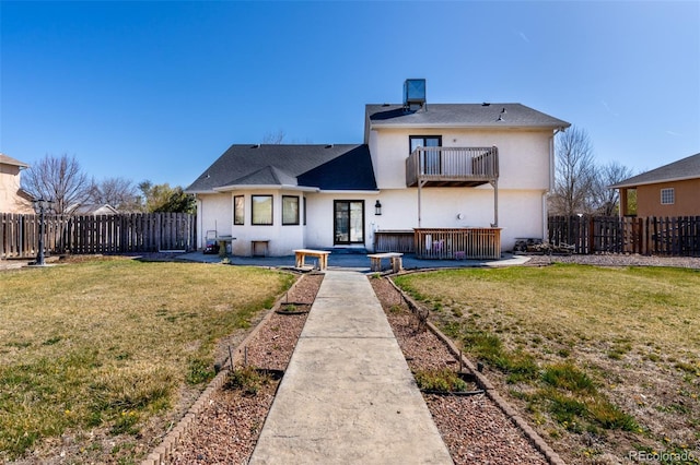 rear view of property featuring a yard, a fenced backyard, stucco siding, and a balcony