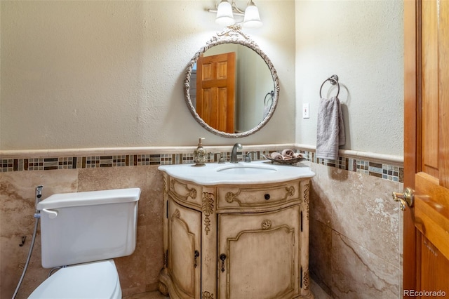 half bath with vanity, wainscoting, tile walls, and toilet