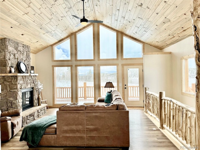 living area with high vaulted ceiling, a wealth of natural light, a stone fireplace, and wood finished floors