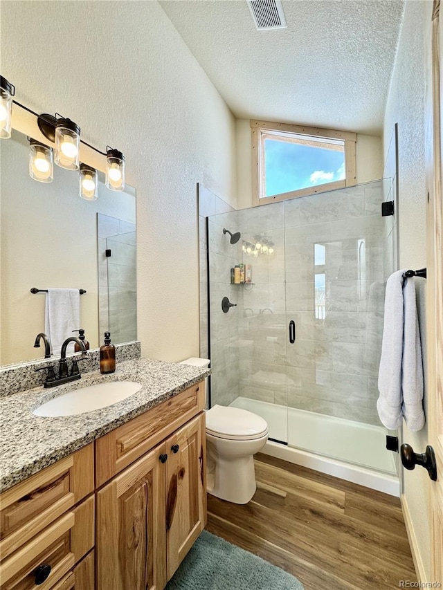 full bath featuring a textured ceiling, toilet, wood finished floors, visible vents, and a shower stall