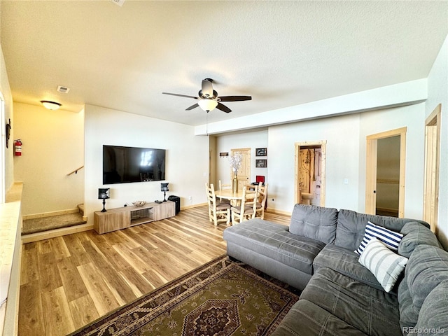 living room featuring baseboards, a ceiling fan, wood finished floors, stairs, and a textured ceiling