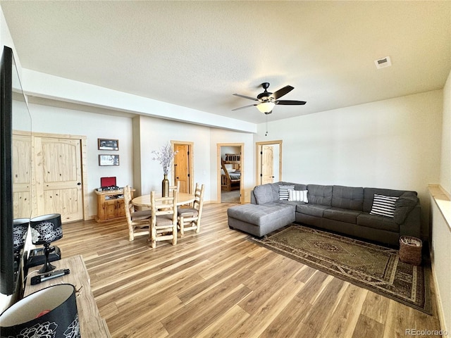 living area featuring light wood-type flooring, visible vents, ceiling fan, and a textured ceiling