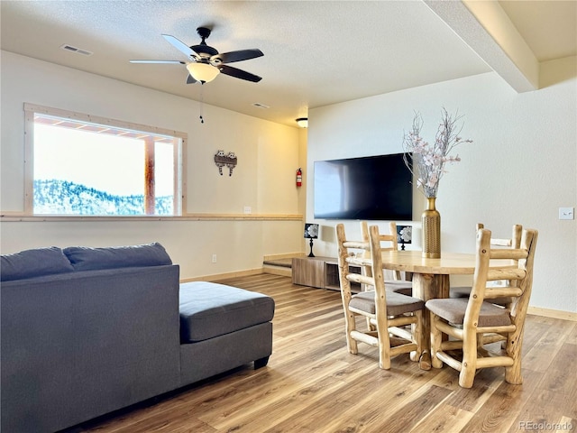 living area with a textured ceiling, a ceiling fan, baseboards, visible vents, and light wood-style floors