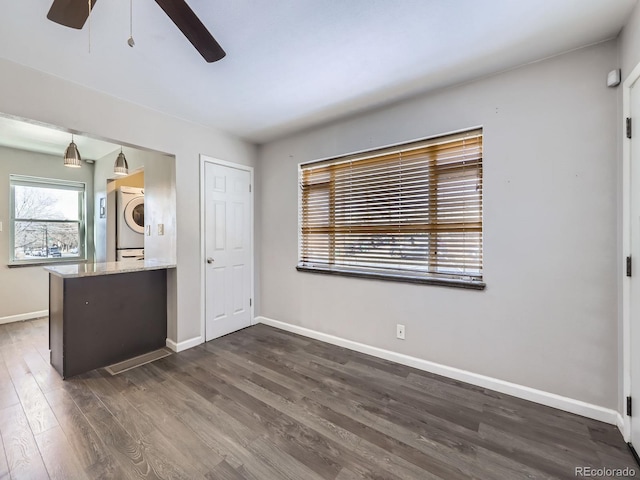 unfurnished bedroom featuring stacked washer and clothes dryer, dark wood-type flooring, and ceiling fan