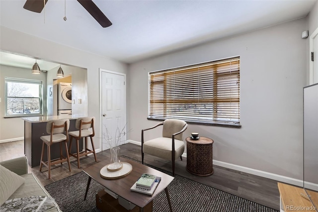 living room featuring dark wood-type flooring, ceiling fan, and stacked washer / dryer