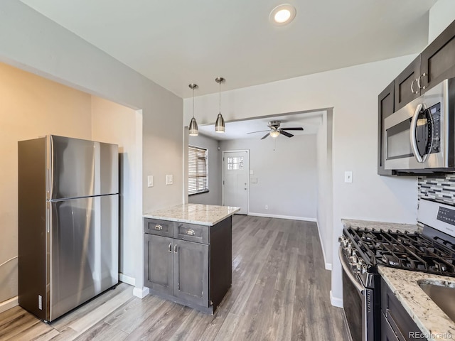 kitchen featuring light stone counters, appliances with stainless steel finishes, light wood-type flooring, and pendant lighting