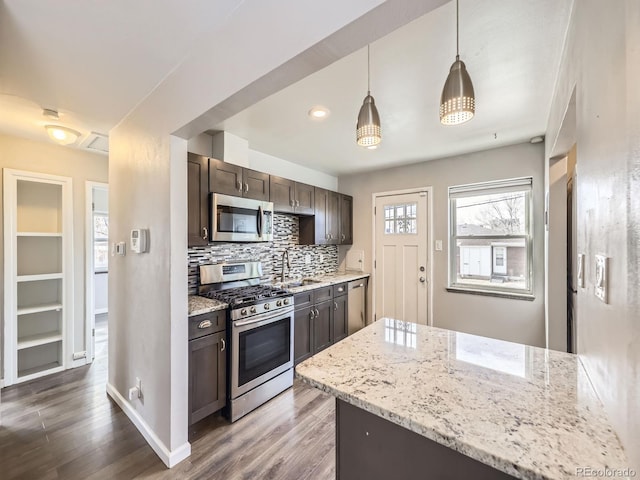 kitchen with appliances with stainless steel finishes, decorative backsplash, hanging light fixtures, light stone counters, and dark brown cabinets