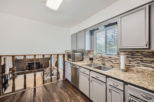 kitchen with gray cabinetry, a sink, tasteful backsplash, stainless steel appliances, and dark wood-style flooring