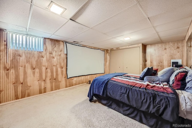 carpeted bedroom with a paneled ceiling and wood walls