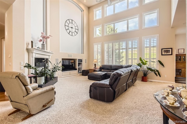 carpeted living room featuring a glass covered fireplace, baseboards, and a towering ceiling