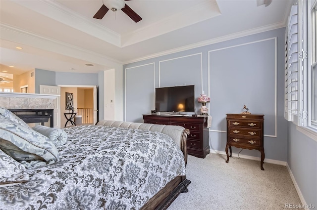 bedroom with a raised ceiling, crown molding, a tiled fireplace, and carpet