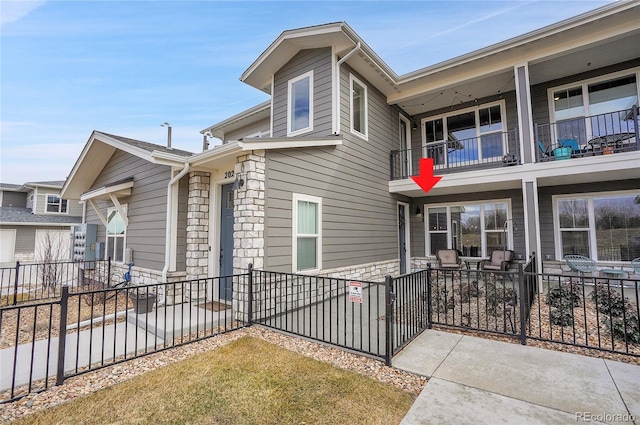 view of front of property featuring a patio area, a balcony, fence, and stone siding