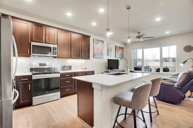 kitchen featuring light wood-style flooring, a sink, open floor plan, stainless steel appliances, and light countertops