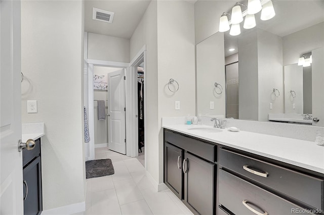 bathroom with tile patterned flooring, visible vents, a walk in closet, baseboards, and vanity