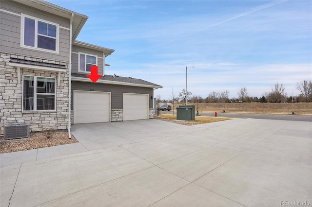 view of home's exterior featuring stone siding, central AC unit, and concrete driveway