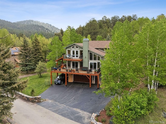 4230 S Meadow Brook Ln, Evergreen, CO 80439 - view of front facade with asphalt driveway, a wooded view, a deck with mountain view, a chimney, and an attached garage
