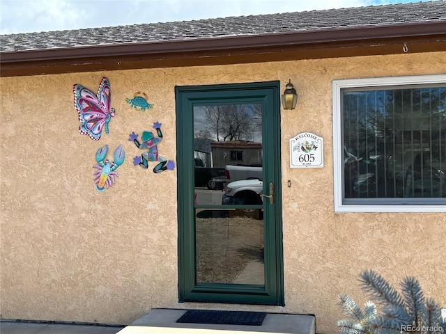 doorway to property featuring stucco siding and roof with shingles