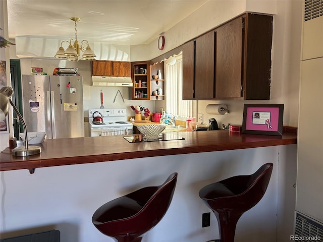 kitchen with a chandelier, under cabinet range hood, electric range, freestanding refrigerator, and dark countertops