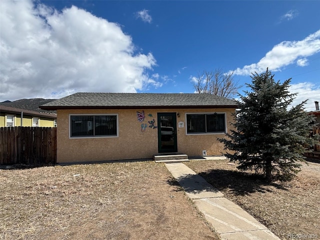 view of front of property featuring a shingled roof, fence, and stucco siding