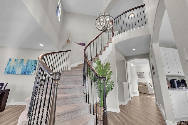 stairway with an inviting chandelier, hardwood / wood-style flooring, and a towering ceiling