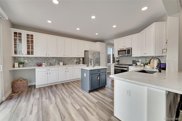 kitchen with sink, appliances with stainless steel finishes, white cabinetry, light stone counters, and a kitchen island