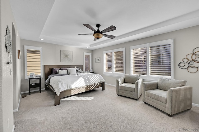 carpeted bedroom with ceiling fan and a raised ceiling