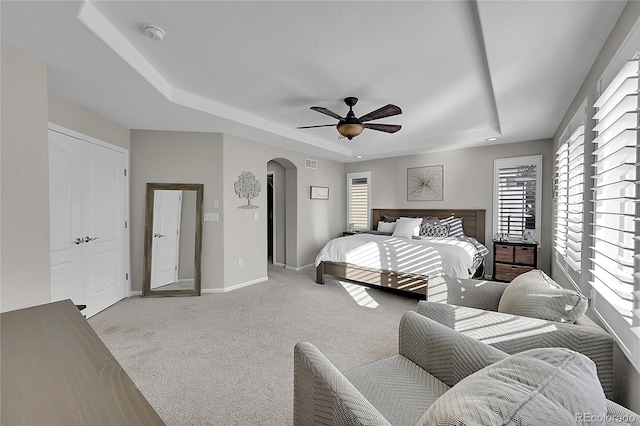 carpeted bedroom featuring a raised ceiling and ceiling fan