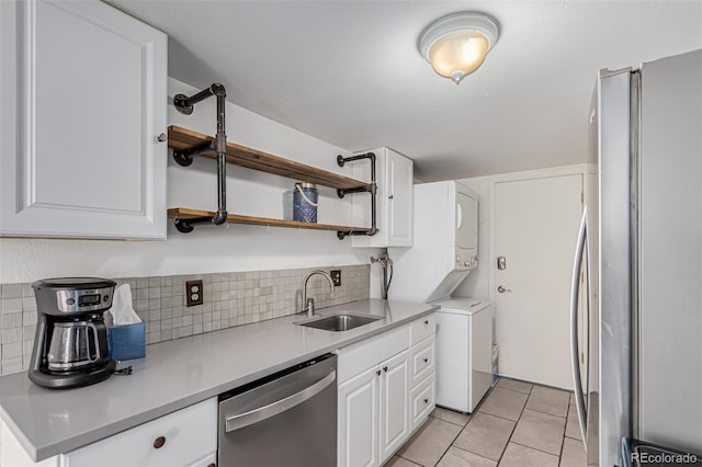 kitchen with sink, appliances with stainless steel finishes, white cabinets, stacked washing maching and dryer, and backsplash