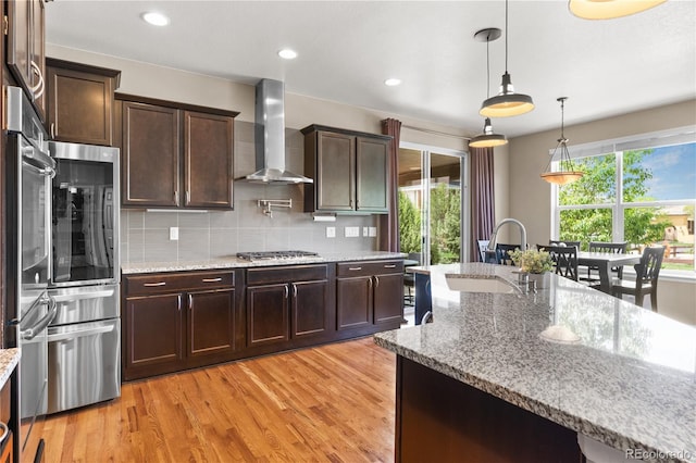1852 E Sea Drift Dr, Windsor, CO 80550 - kitchen featuring wall chimney range hood, stainless steel appliances, light wood-style flooring, dark brown cabinets, and recessed lighting