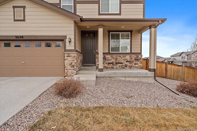 view of front of home with stone siding, covered porch, fence, and concrete driveway