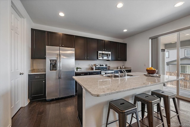 kitchen with dark brown cabinetry, dark wood finished floors, a breakfast bar area, stainless steel appliances, and recessed lighting